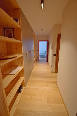 A hallway with wooden shelving units, a bed in the distance, and a door on the right. - CROZZON view Apartment MhD (Madonna di Campiglio)