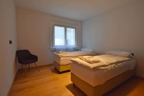 Ein Zimmer mit zwei Betten, einem Sessel und einem Fenster.