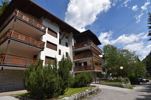 A multi-story building with balconies, a stone wall, and a paved area with trees. - CROZZON view Apartment MhD (Madonna di Campiglio)