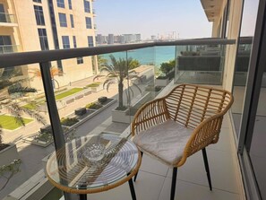 Ein Balkon mit Korbmöbeln, einem Glastisch und Blick auf einen Yachthafen sowie Gebäude.