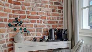 Een wit bureau met een koffiezetapparaat, kopjes en een vaas met bladeren voor een bakstenen muur.