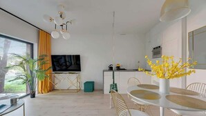 Una sala de estar moderna con televisor, mesa de comedor, sillas y una planta.