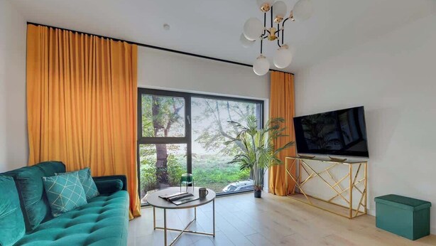 Una sala de estar moderna con un sofá color turquesa, una mesa de centro redonda, un televisor sobre un mueble de madera y un amplio ventanal con cortinas.