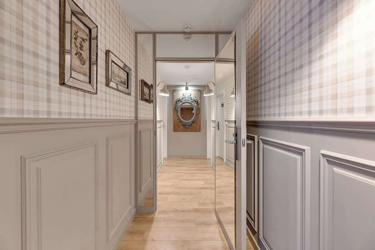 Ein Korridor mit kariertem Wanddesign, gerahmten Bildern, einem Spiegel und einem Holzboden.