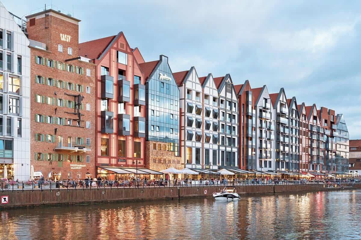 Ein Hotel am Wasser mit einer Reihe traditioneller Gebäude im europäischen Stil, einem Restaurant im Erdgeschoss und einem Boot, das im Wasser liegt.
