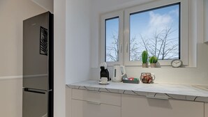 Eine moderne Küche mit Einbaukühlschrank, einer Kaffeemaschine und einem Fenster mit Blick auf kahle Bäume.