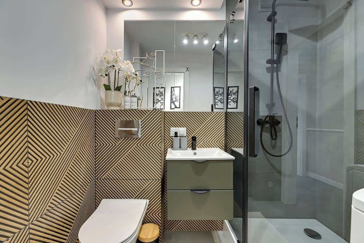 Un baño moderno con pared de diseño geométrico, un lavabo blanco, un espejo y zona de ducha.