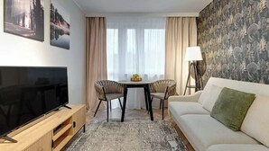 Ein Wohnzimmer mit Flachbildfernseher, einer Couch, einem Couchtisch, zwei Sessel, einer Lampe und einer Wand mit Muster.