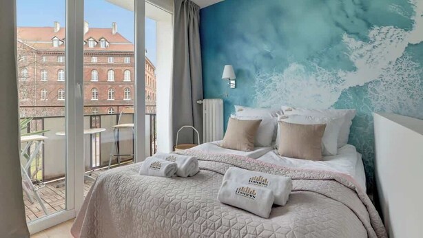 A hotel room with a large bed, a view of a building through a glass door, and a blue wall with a wave pattern. - Old Town Sieroca | Comfortable Stay (Gdańsk)
