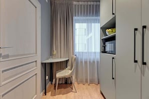 Ein kleines, kompaktes Zimmer mit Esstisch, Stuhl, Fenster mit leichtem Vorhang und Einbauschränken.