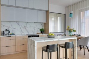 A modern kitchen with marble countertops, wooden cabinets, and a central island with bar stools. - Brabank 10 | Riverside & Balcony | Parking (Gdańsk)
