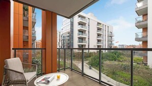 En balkon med fletstole og et bord, med udsigt over et boligområde med moderne bygninger.
