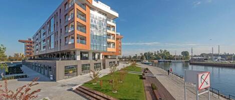 A modern multi-story building with a glass facade, a waterfront view, and a pedestrian walkway.