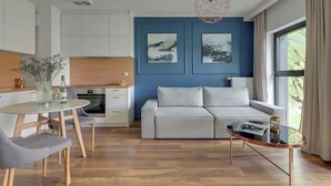 A modern living room with a sofa, a dining table with chairs, a coffee table, and artwork on the wall. - Rezydencja Wintera 11 | Riverside (Gdańsk)