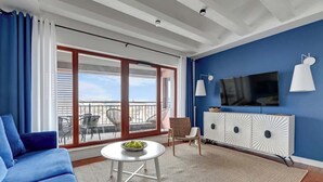 A modern living room with a blue sofa, a round table with a bowl, a TV on the wall, and a balcony with outdoor furniture. - N º 96 with Balcony | Pool & SPA | River View (Gdańsk)