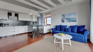 A modern kitchen with white cabinets, a dining area with a blue sofa and a white coffee table, and a large window with a view of the sea. - Nº 96 with Balcony | Pool & SPA | River View (Gdańsk)