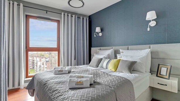 A bedroom with a large bed, a nightstand, a wall-mounted lamp, and a window with curtains. - Nº 96 with Balcony | Pool & SPA | River View (Gdańsk)