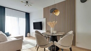 Un soggiorno moderno con un divano, un tavolo da pranzo con sedie, una TV a parete e un pannello decorativo.