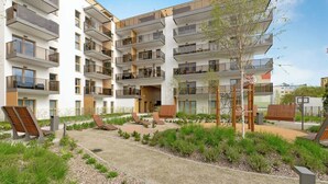 Un edificio residenziale a più piani con balconi, un cortile con posti a sedere e un piccolo albero.