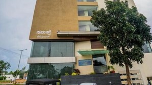 Un edificio de varios pisos con un llamativo logotipo 'S', un porche cubierto y un árbol en primer plano.