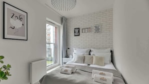 Een moderne slaapkamer met een witte baksteenmuur, een lijstwerk met kunst, een bed met wit beddengoed en een raam met uitzicht.