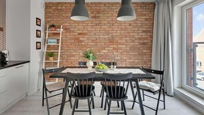 Een moderne keuken met een bakstenen muur, een eettafel met stoelen, hanglampen en uitzicht op de straat.