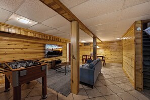 A cozy room with wooden walls, a foosball table, a sofa, and a television.