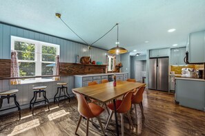 A modern kitchen with a wooden dining table, orange chairs, and a large window.