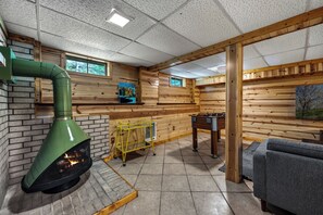 A cozy room with a fireplace, a foosball table, and a window with a view of trees.