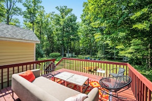 A deck with outdoor furniture, a small table, and a view of a wooded area.