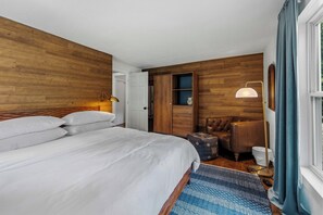 A hotel room with a large bed, a wardrobe, a seating area, and a window with curtains.