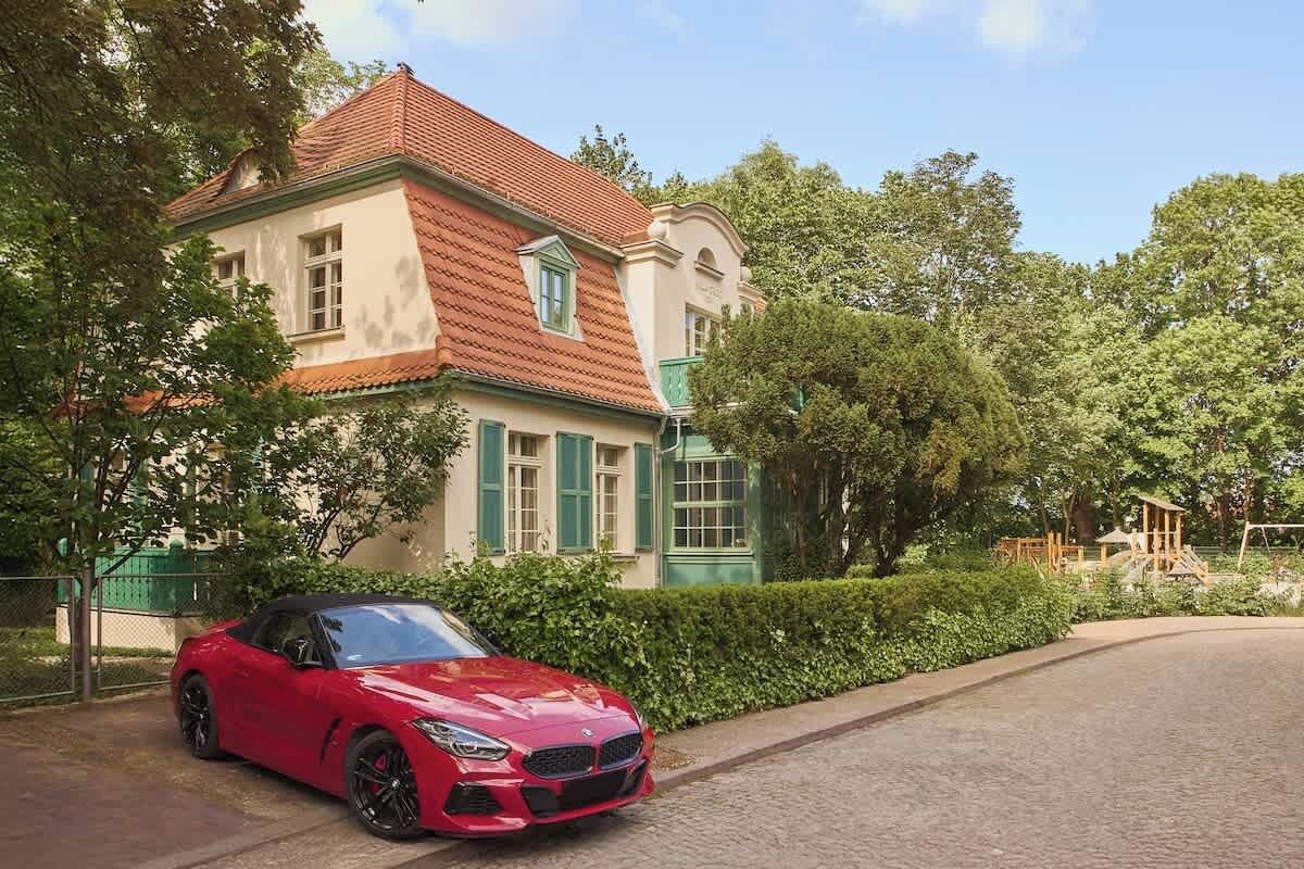 Ein roter Sportwagen vor einem großen, historischen Gebäude mit rotem Ziegeldach und grünen Fensterläden.