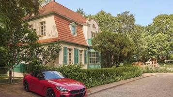 Ein roter Sportwagen vor einem großen, historischen Gebäude mit rotem Ziegeldach und grünen Fensterläden.