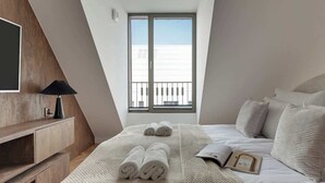 Ein Schlafzimmer mit einem Bett, Kissen, einem Nachttisch, einer Lampe und einem Fenster.
