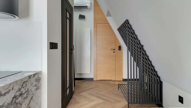 Een modern interieur met een visgraatvloer, een trap met een metalen leuning, en een deur die leidt naar een andere kamer.