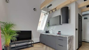 Een moderne keuken met een ingebouwde televisie, grijze kastjes, een marmeren werkblad en een groot raam.