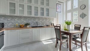 A modern kitchen with white cabinets, a tiled backsplash, and a dining area with a wooden table and chairs. - Piwna Sunlight | Old Town | 2 Bedrooms (Gdańsk)