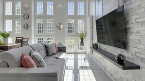 A modern living room with a large TV, white walls, and a brick accent wall. - Piwna Sunlight | Old Town | 2 Bedrooms (Gdańsk)