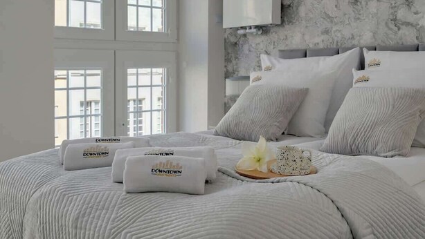 A hotel room with a large bed, multiple pillows, a nightstand, and a view of buildings through the window. - Piwna Sunlight | Old Town | 2 Bedrooms (Gdańsk)