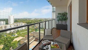 Ein Balkon mit Korbmöbeln, einem Tisch mit Frühstücksangeboten und Blick auf Gebäude und Grünflächen.