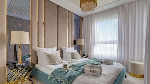 Ein modernes Hotelzimmer mit einem großen Bett, zwei Nachttischen, einer Chandelüster und Blick auf die Stadt.