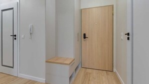 A hallway with a white door, a wooden door, and a small wooden shelf. - Latarników 84 | Perfect Stay (Gdańsk)