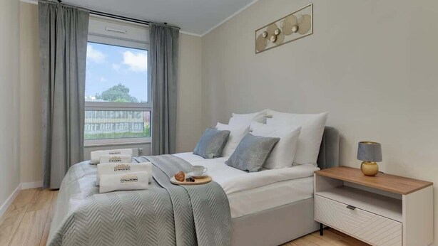 A neatly arranged bedroom with a bed, bedside table, and a view through the window. - Latarników 84 | Perfect Stay (Gdańsk)