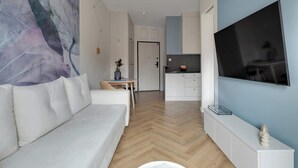 A modern living room with a sofa, a dining table, a kitchen area, and a TV mounted on the wall. - Granaria D507 | Best Location (Gdańsk)