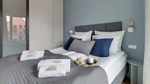 A hotel room with a large bed, a bedside table, a nightstand, a window, and a view of buildings outside. - Granaria D507 | Best Location (Gdańsk)