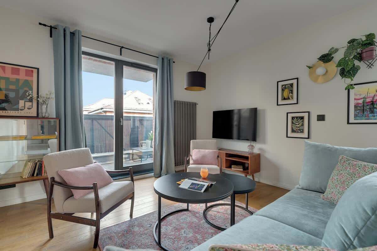 Una sala de estar moderna con un sofá, sillones, una mesa de centro, un televisor de pantalla plana y un amplio ventanal con cortinas.