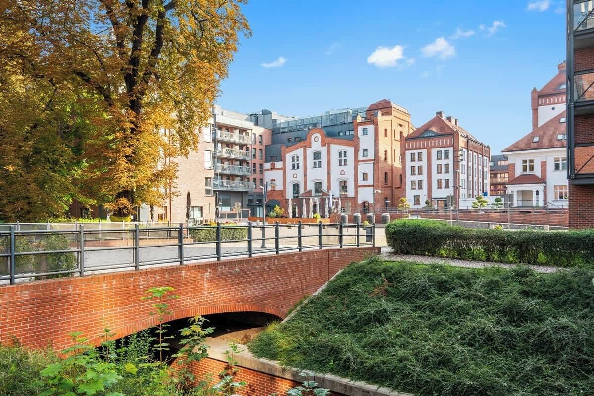 Een bakstenen brug over een gracht, met gebouwen op de achtergrond.