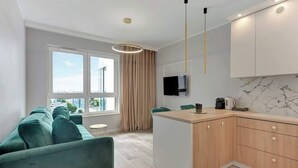 Een moderne keuken met een televisie, een zithoek met een groene bank en een groot raam met uitzicht op de stad.