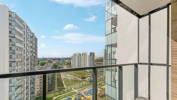 Een hoog gebouw met een balkon, met uitzicht op een speeltuin en andere gebouwen.