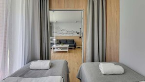 Ett hotellrum med två sängar, ett trägolv, en soffa och utsikt genom en glasdörr.